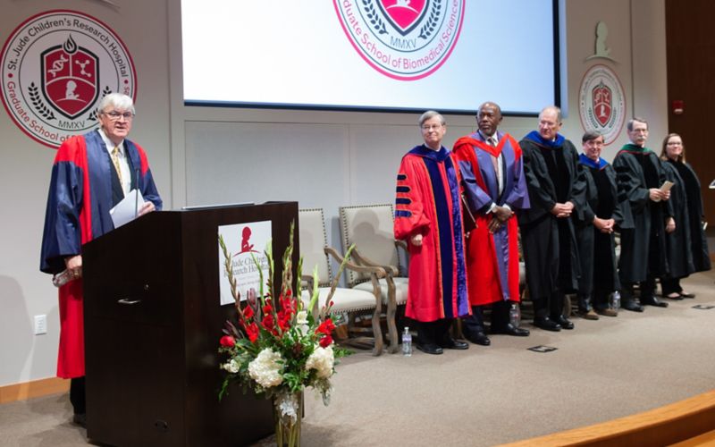 Man at podium, other people standing to his left.