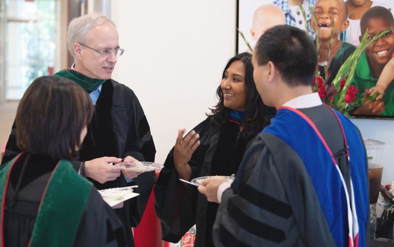 Four people in academic regalia talking