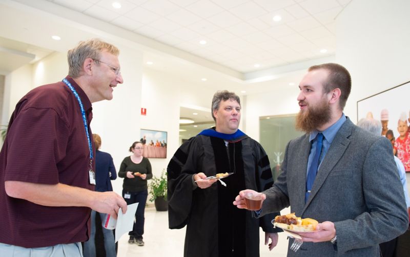 Three people talking. Bearded man on right.