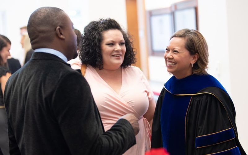 Woman in academic regalia talks to students