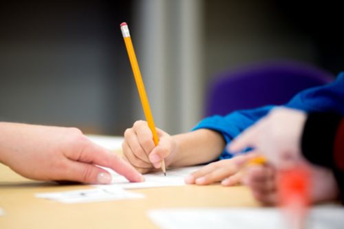 Child holding pencil while writing at desk. 