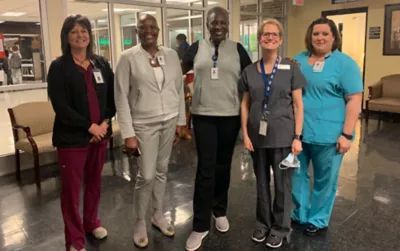 Diverse health care team of five medical professionals standing together in hospital hallway, including nurses and staff members wearing ID badges