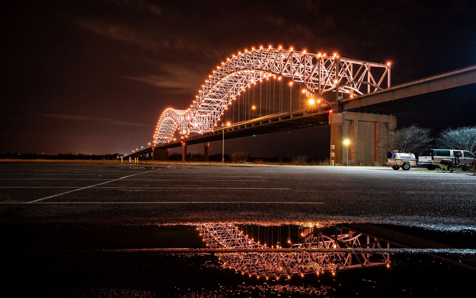 View from a parking lot of the Hernando De Soto Bridge lit up at night.