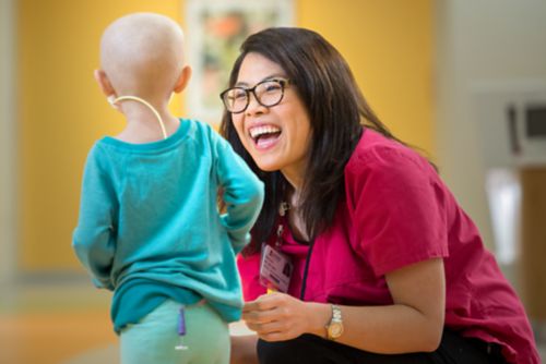 Smiling nurse stooped and interacting with very young cancer patient.