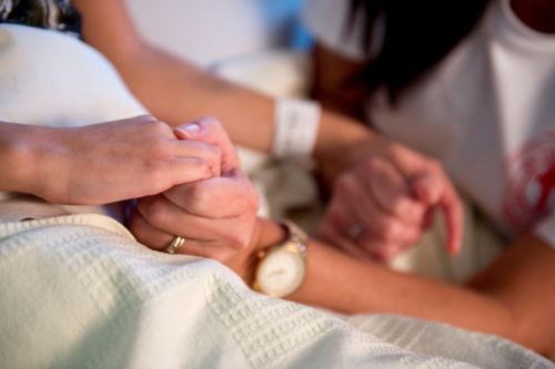 Caregiver holds hands with a pediatric cancer patient