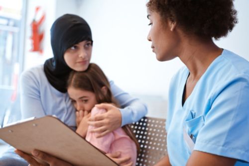 Woman embracing daughter while looking at nurse