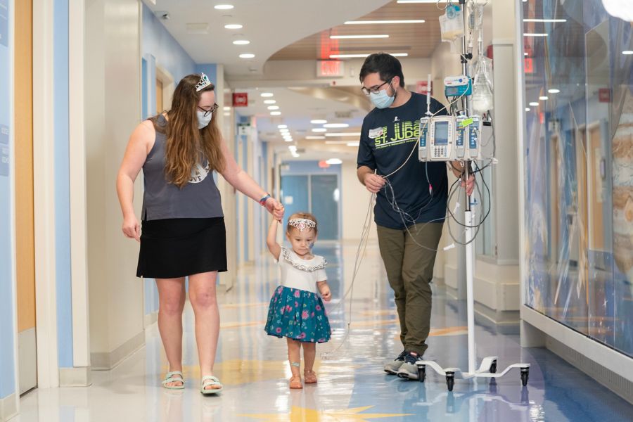 Mother and father walk with small female child in hallway of hospital