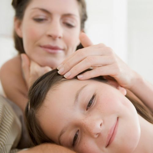 Mother gently stroking daughter's hair while child rests peacefully, nurturing parent-child moment showing care and comfort in home setting