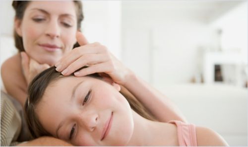 A mother caring for her daughter with her hand resting on the young girl's forehead.