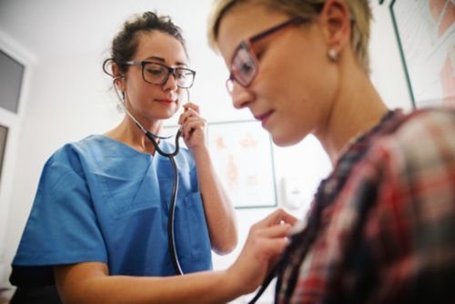 Female doctor listening to female patient's heart with stethoscope