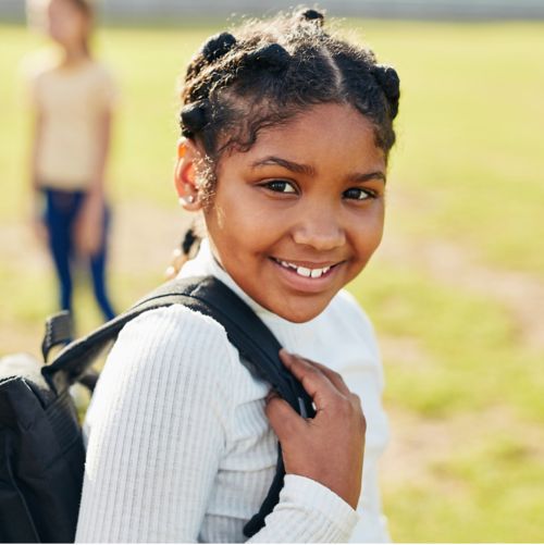 image of young girl smiling, carrying a backpack