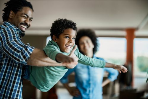 A child pretending to fly in the arms of an adult.