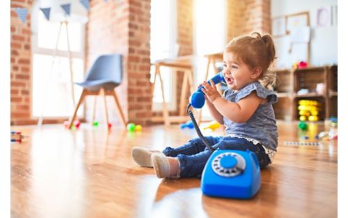 Female toddler playing on hardwood floor with toy phone