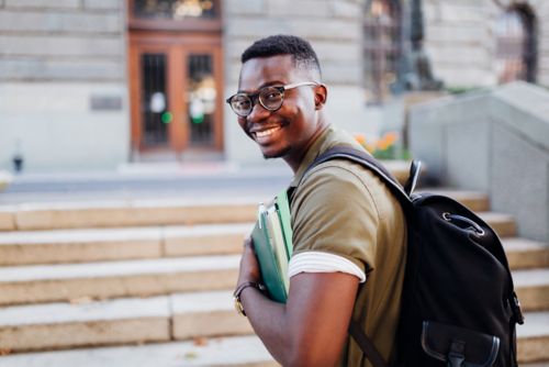 young man w/books outside library-ish building