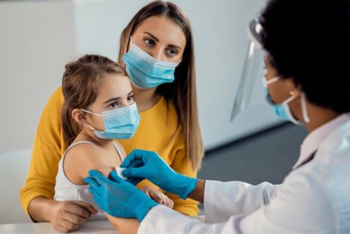 Mãe jovem segura a filha enquanto a criança recebe uma injeção do médico.