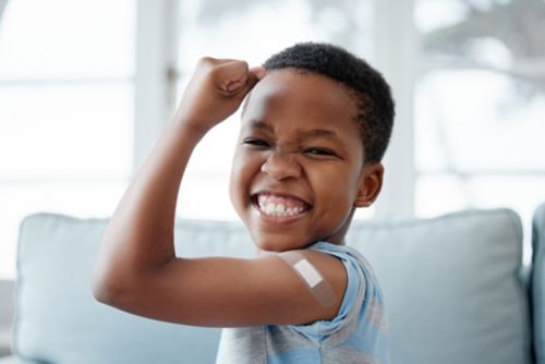 Male child holding arm up with big smile after being vaccinated