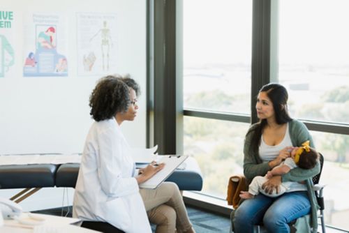 Mom holding child while talking with doctor.