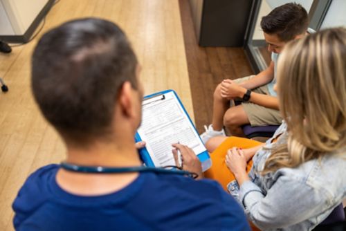 urse receptionist explains paperwork to a woman with her son at the doctors office waiting room lobby