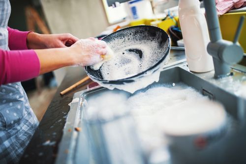 Woman cleaning black nonstick pan in sink with soapy water