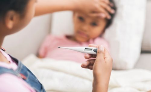 Mother taking temperature of daughter lying in bed with thermometer.