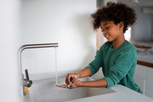 Female child washes hands in sink.