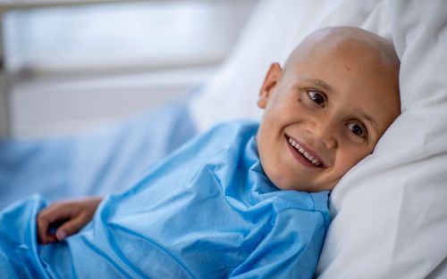 Young boy with shaved head smiling in hospital bed