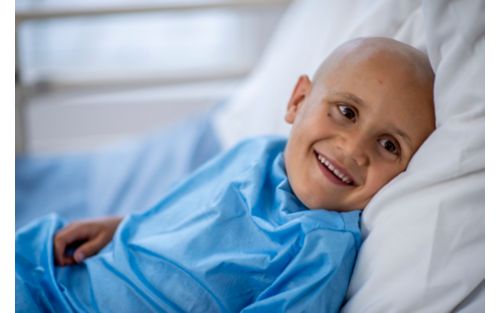 Young boy with shaved head smiling in hospital bed