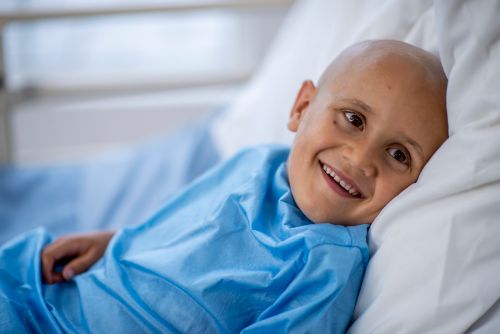 Young boy with shaved head smiling in hospital bed