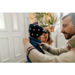 Father helps small child put on winter coat and hat