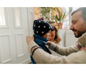 Father helps small child put on winter coat and hat