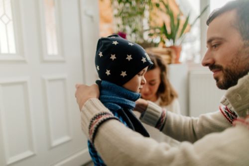 Father helping small child put on winter coat and hat