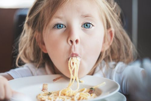Little girl eating bowl of spaghetti.