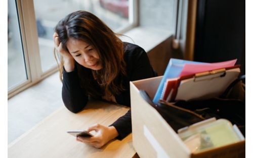 Woman looking at phone with box of office items beside her