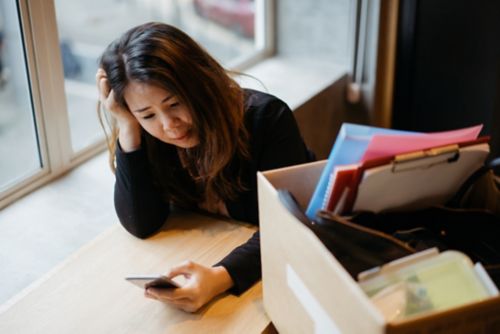 Woman looking at phone with box of items beside her