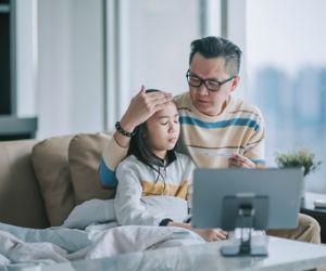  father taking temperature for his sick daughter on sofa living room videocall with his doctor via digital tablet