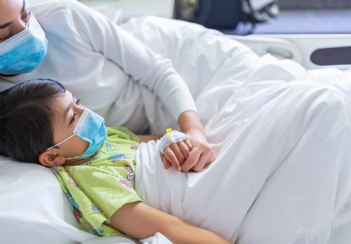 Sick child lying in hospital bed with mother holding hand