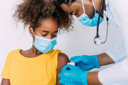 Masked doctor puts on Band-Aid for a female child.