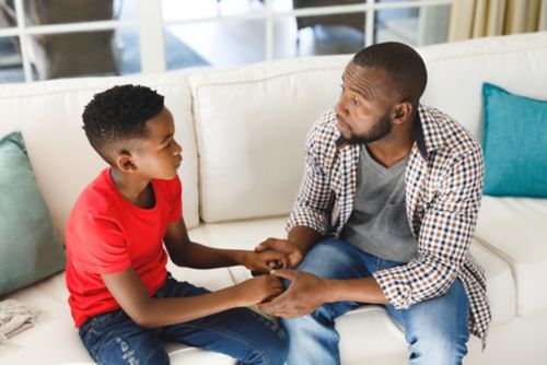 Father discussing serious matter with son while holding hands on couch.
