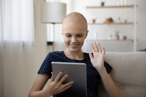 Young woman with cancer chatting with friends on video call holding tablet