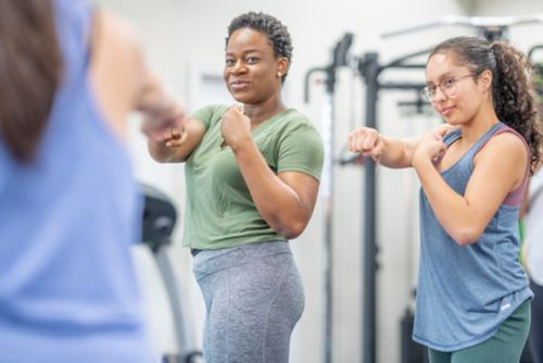 A small group women stand with their fists up as they participate in a boxing class.