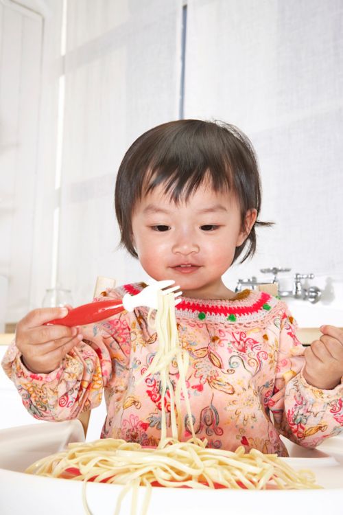 Toddler eating spaghetti with child-friendly fork.