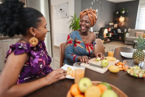 Two African women eating fruit at kitchen table