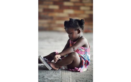 Little girl sits down while putting on shoes.