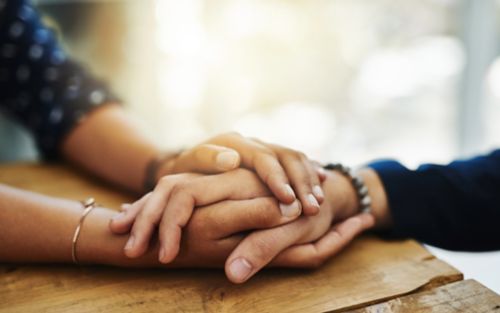 Closeup of two unrecognizable people holding hands in comfort