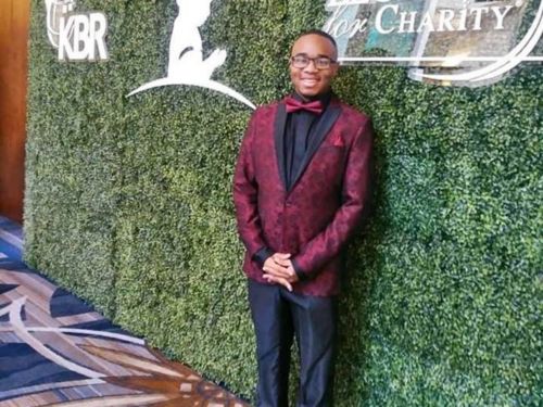 Javon wearing a tuxedo standing in front of a green wall.