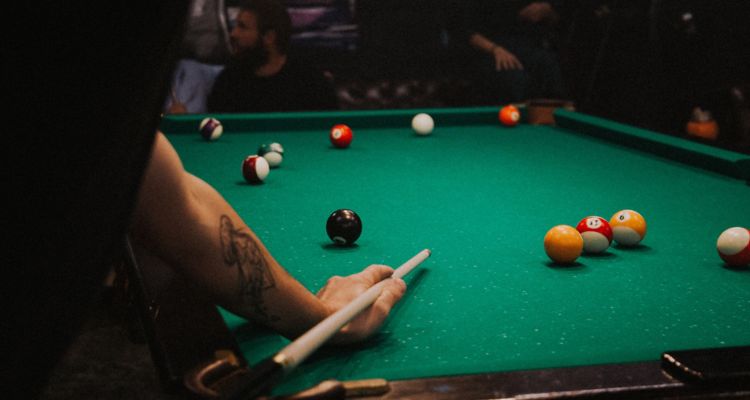 Photo of pool table, someone w/tattoo holding pool cue
