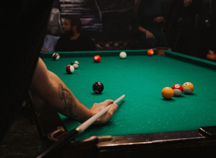 Photo of pool table, someone w/tattoo holding pool cue