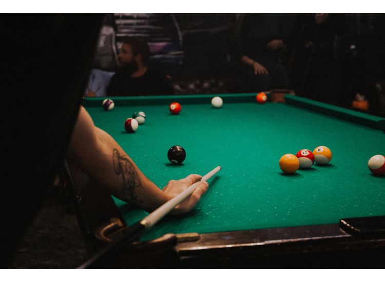 Photo of pool table, someone w/tattoo holding pool cue