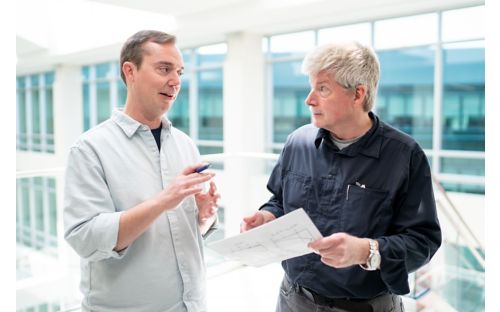 two men talking one is holding a report