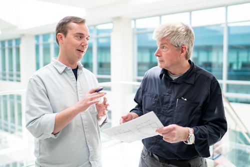 two men talking in an atrium sort of hallway. 